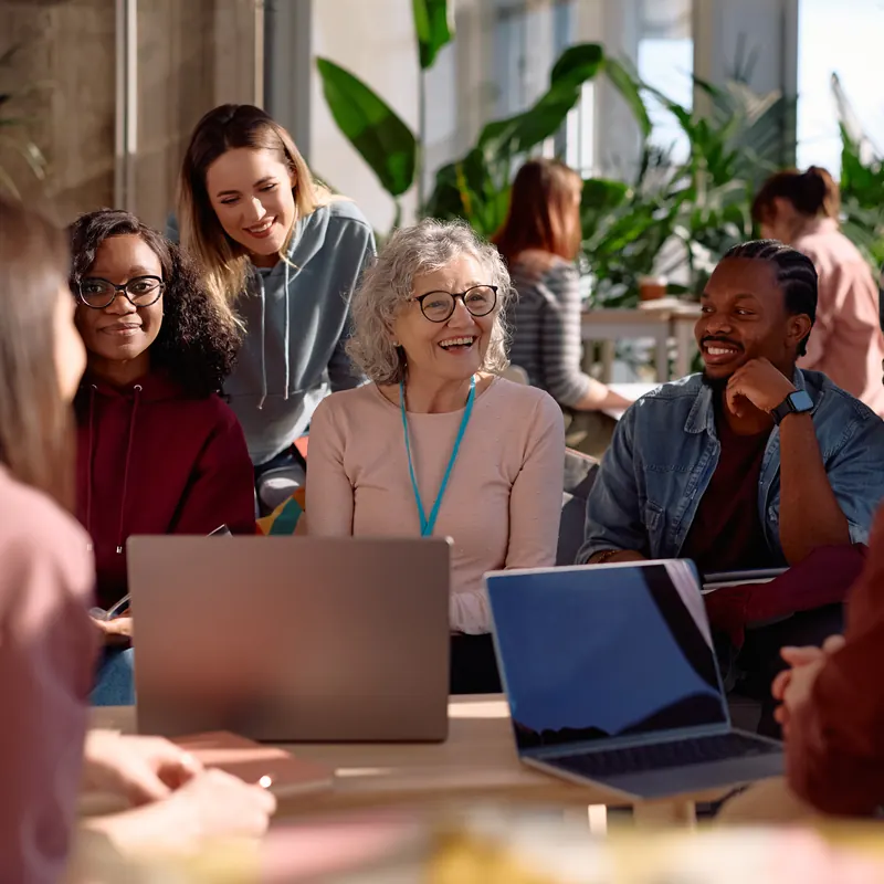A mixed-age group talking and laughing around a table with laptops